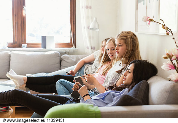 Side view of teenage girls watching TV while relaxing on sofa at home