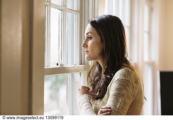 Side view of thoughtful woman standing by window at home