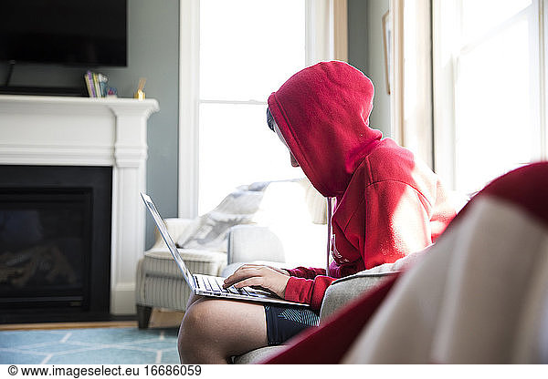 Side View of Tween Boy in Hooded Sweatshirt Working on Laptop Computer