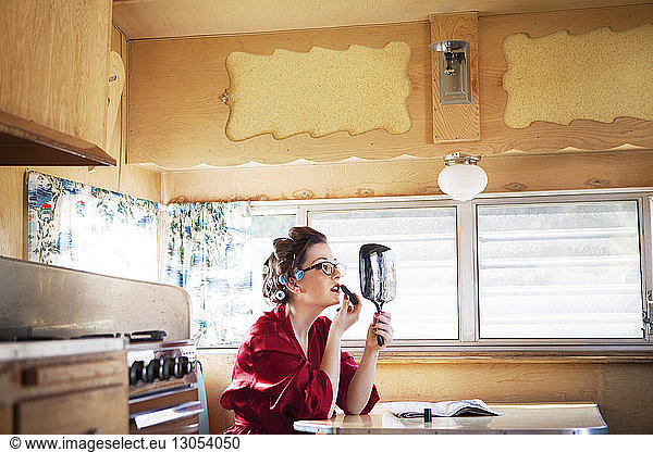 Side view of woman applying lipstick while sitting by table in camper van