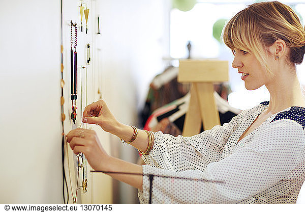 Side view of woman arranging necklace on wall in store