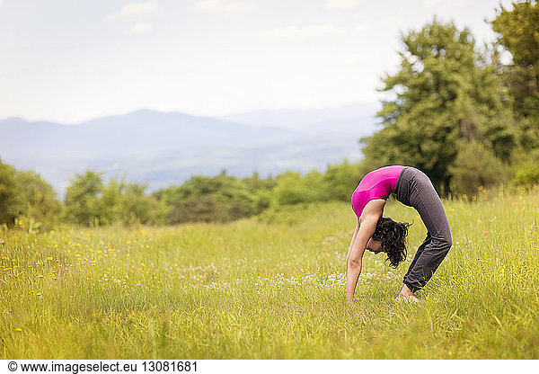 Side view of woman bending over backwards on grassy field