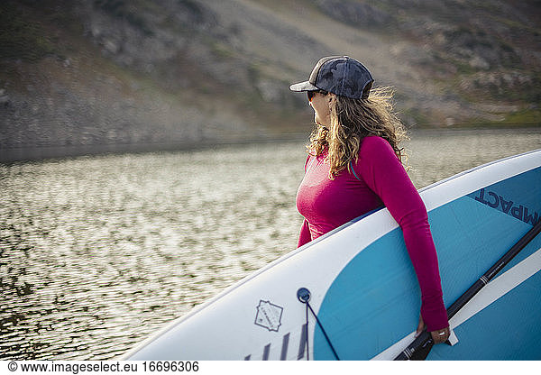 Side view of woman carrying paddleboard by lake