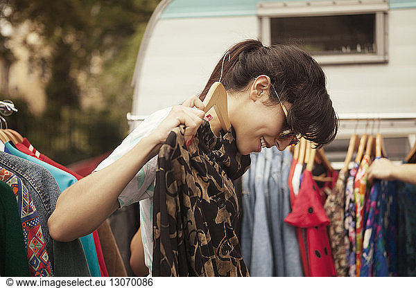 Side view of woman checking dress while standing by clothes rack