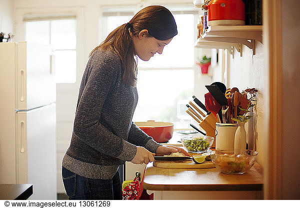 Side view of woman cutting vegetable on cutting board in kitchen at home