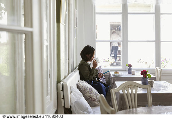 Side view of woman drinking coffee and using phone while resting at cafe