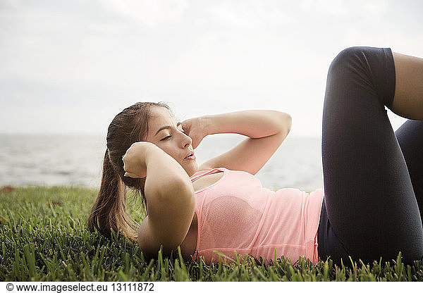 Side view of woman exercising on grassy field on sunny day
