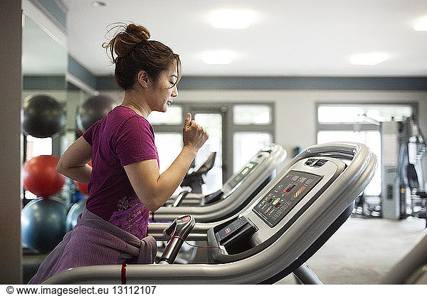 Side view of woman exercising on treadmill at gym