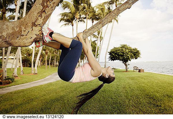 Side view of woman hanging on tree branch at grassy field