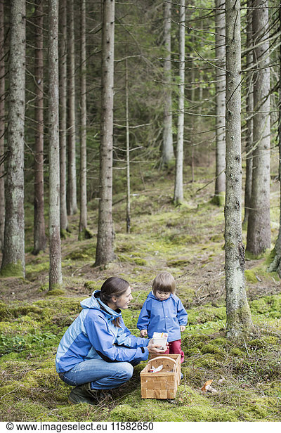 Side view of woman holding food while looking at daughter in forest