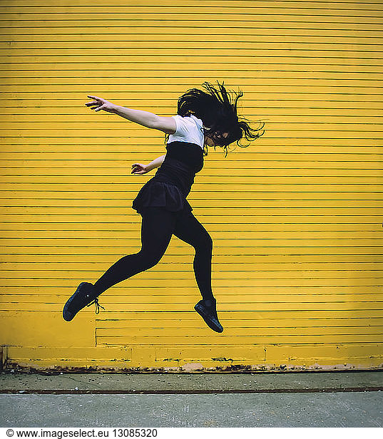 Side view of woman jumping against yellow shutter