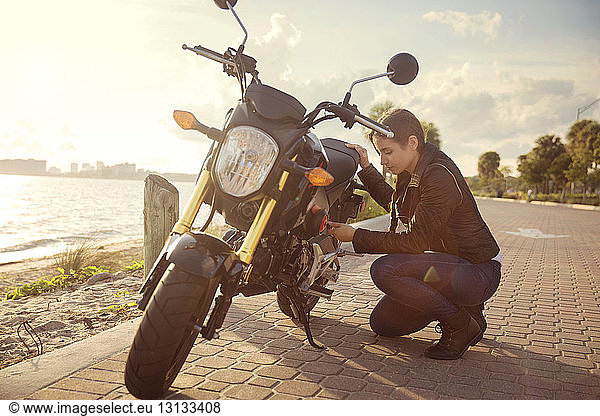 Side view of woman kneeling by motorcycle on street