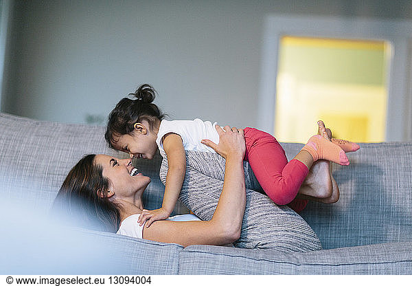 Side view of woman playing with girl on sofa at home