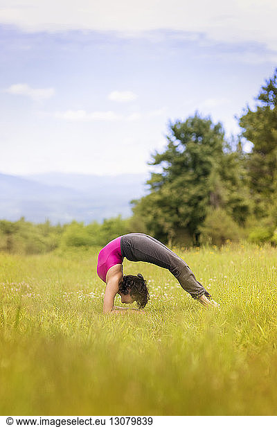 Side view of woman practicing bridge pose yoga on grassy field