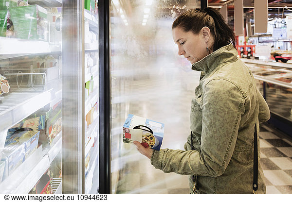 Side view of woman reading food label at refrigerated section