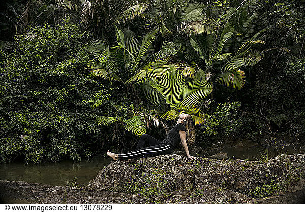 Side view of woman relaxing on rocks at lakeshore in El Yunque National Forest