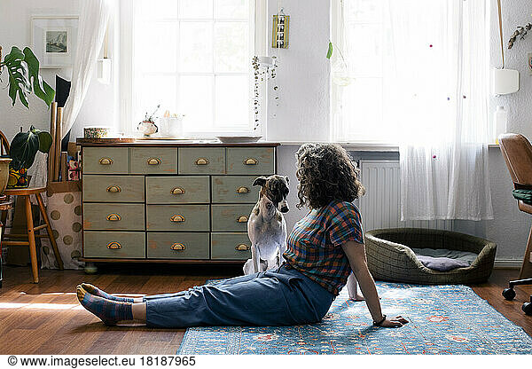 Side view of woman sitting on floor with dog at home