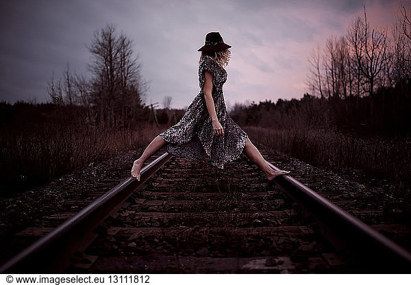 Side view of woman standing on railroad tracks against cloudy sky during sunset