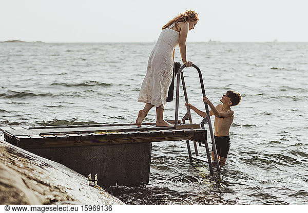 Side view of woman talking while son standing on ladder in sea