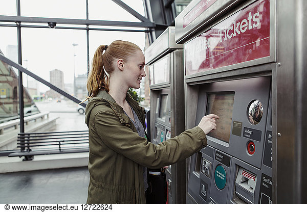 Side view of woman using ticket machine at railroad station
