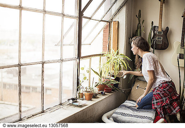 Side view of woman watering potted plants on window at home