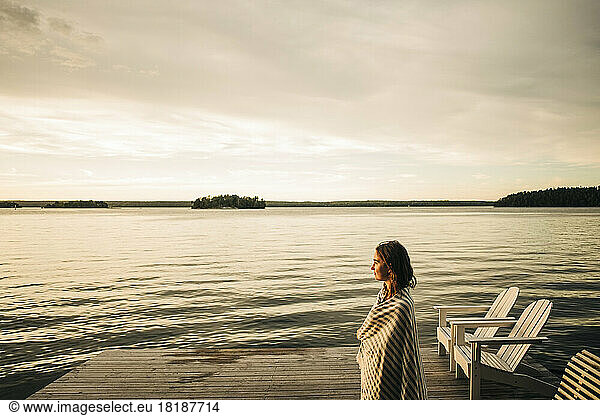 Side view of woman wearing towel while standing on jetty during sunset