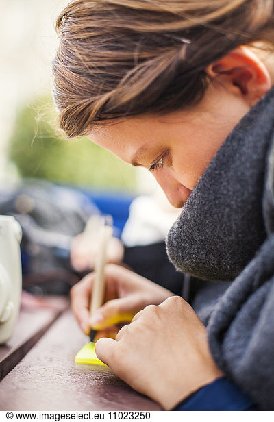 Side view of woman writing on adhesive note outdoors