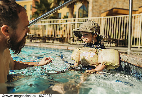 Side view of young boy playing with dad in water in vacation pool