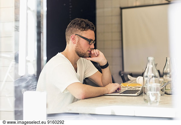 Side view of young businessman using laptop in creative office