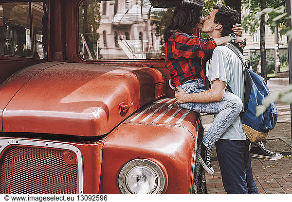 Side view of young couple kissing on mouth in city by vintage bus