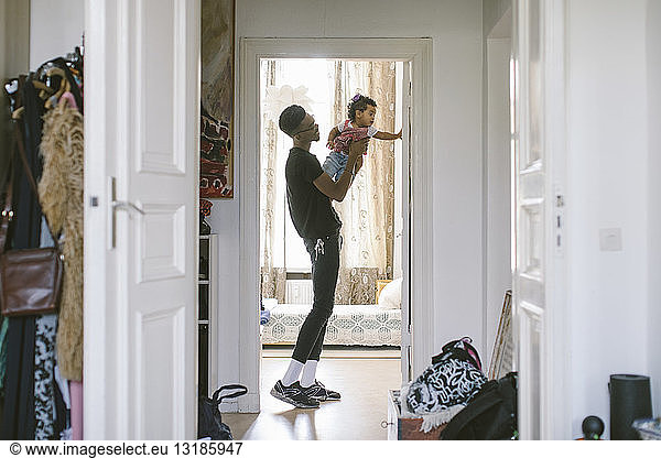 Side view of young man lifting daughter while standing at doorway in house