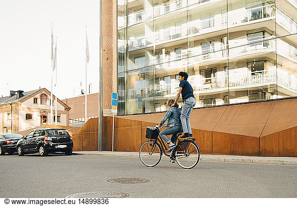 Side view of young man riding bicycle with friend on street in city