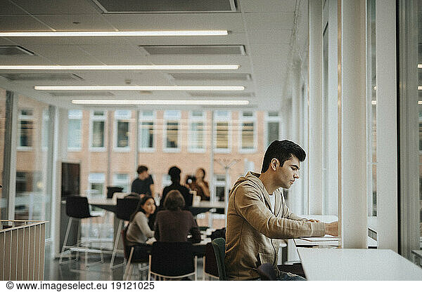Side view of young student studying at table in university