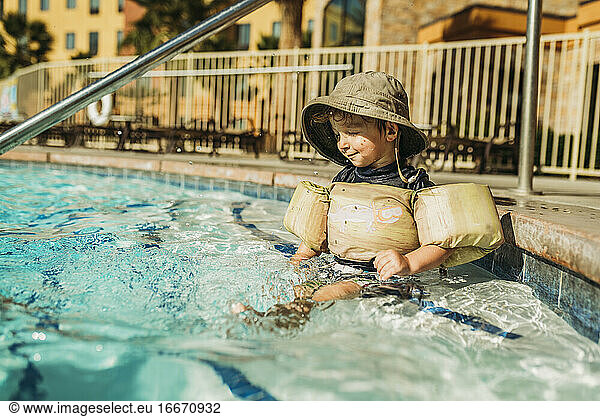 Side view of young toddler boy splashing in water in vacation pool