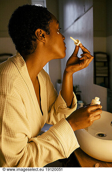 Side view of young woman applying beauty product on face