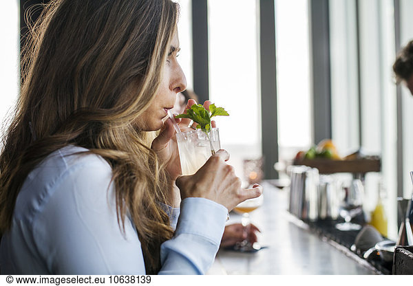 Side view of young woman sipping cocktail at bar counter