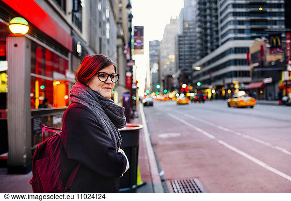 Side view of young woman waiting at sidewalk in city