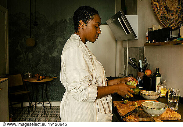 Side view of young woman with grapes at kitchen counter