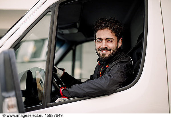 Side view portrait of confident young delivery man driving truck