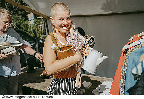 Side view portrait of happy female customer holding various objects while shopping at flea market