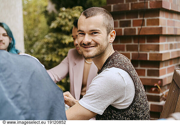 Side view portrait of smiling gay man sitting with friends during party in back yard