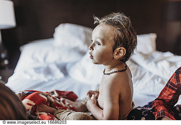 Side view portrait of toddler boy sitting in hotel bed on vacation