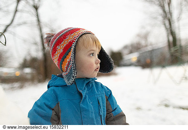 Side view portrait of toddler boy wearing knit hat outdoors in snow