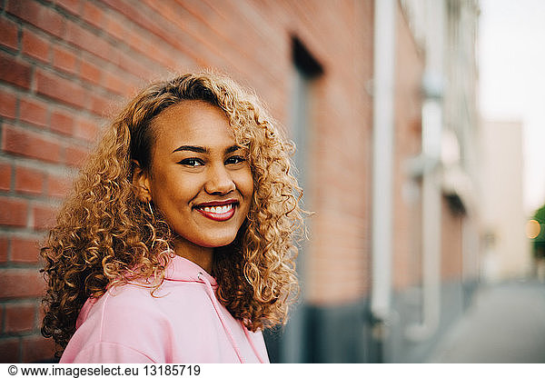Side view portrait of young woman with curly hair against brick wall