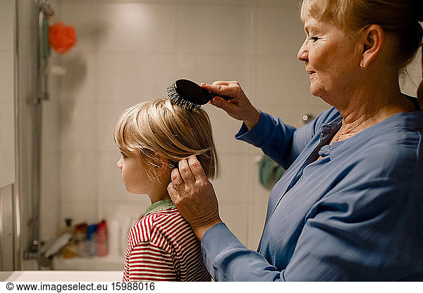 Side view senior woman combing hair of grandson in bathroom at home