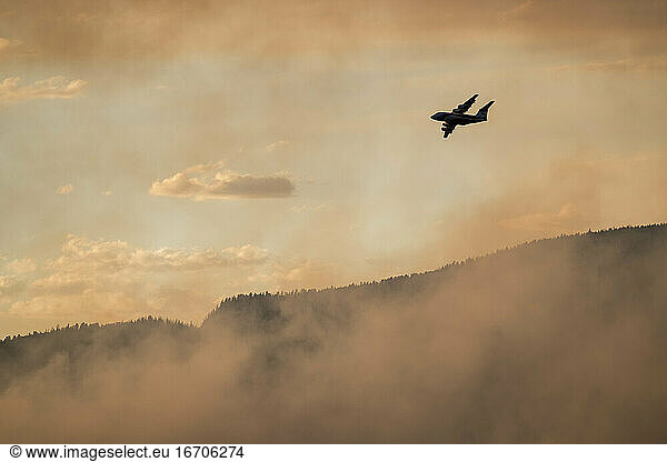 Silhouette airplane flying over smoke emitting from wildfire in forest