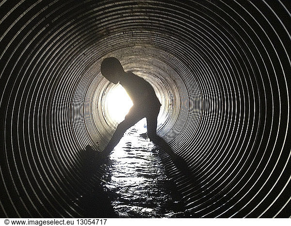 Silhouette boy standing in sewage tunnel