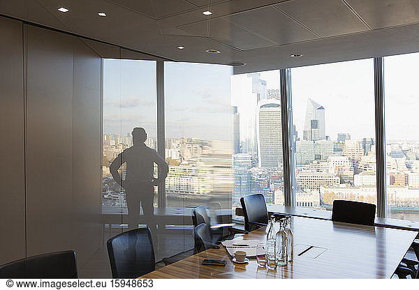 Silhouette businessman standing at urban highrise office window