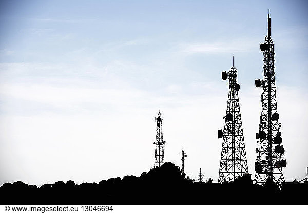 Silhouette communication towers against sky