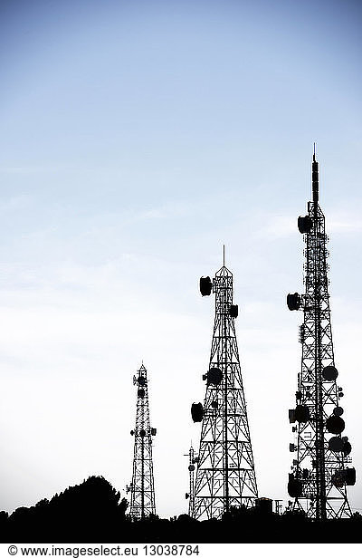 Silhouette communication towers against sky during sunset